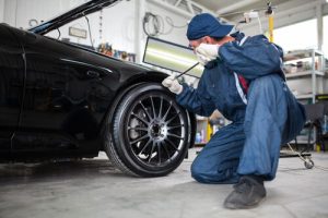 Mechanic inspecting the wheel of a black car in a garage.